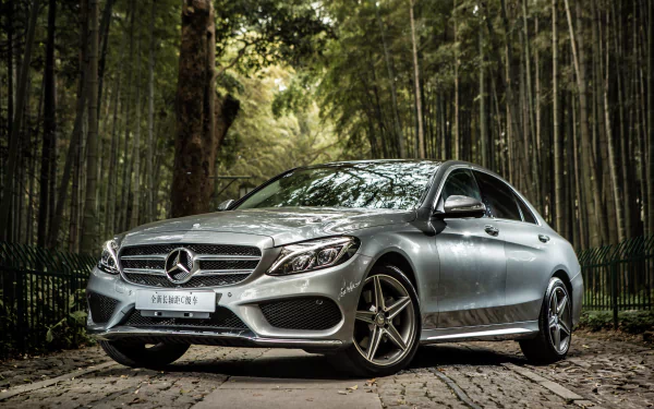 Silver Mercedes-Benz C-Class parked on a cobblestone path surrounded by tall trees, captured in sharp 4K Ultra HD as a desktop wallpaper background.