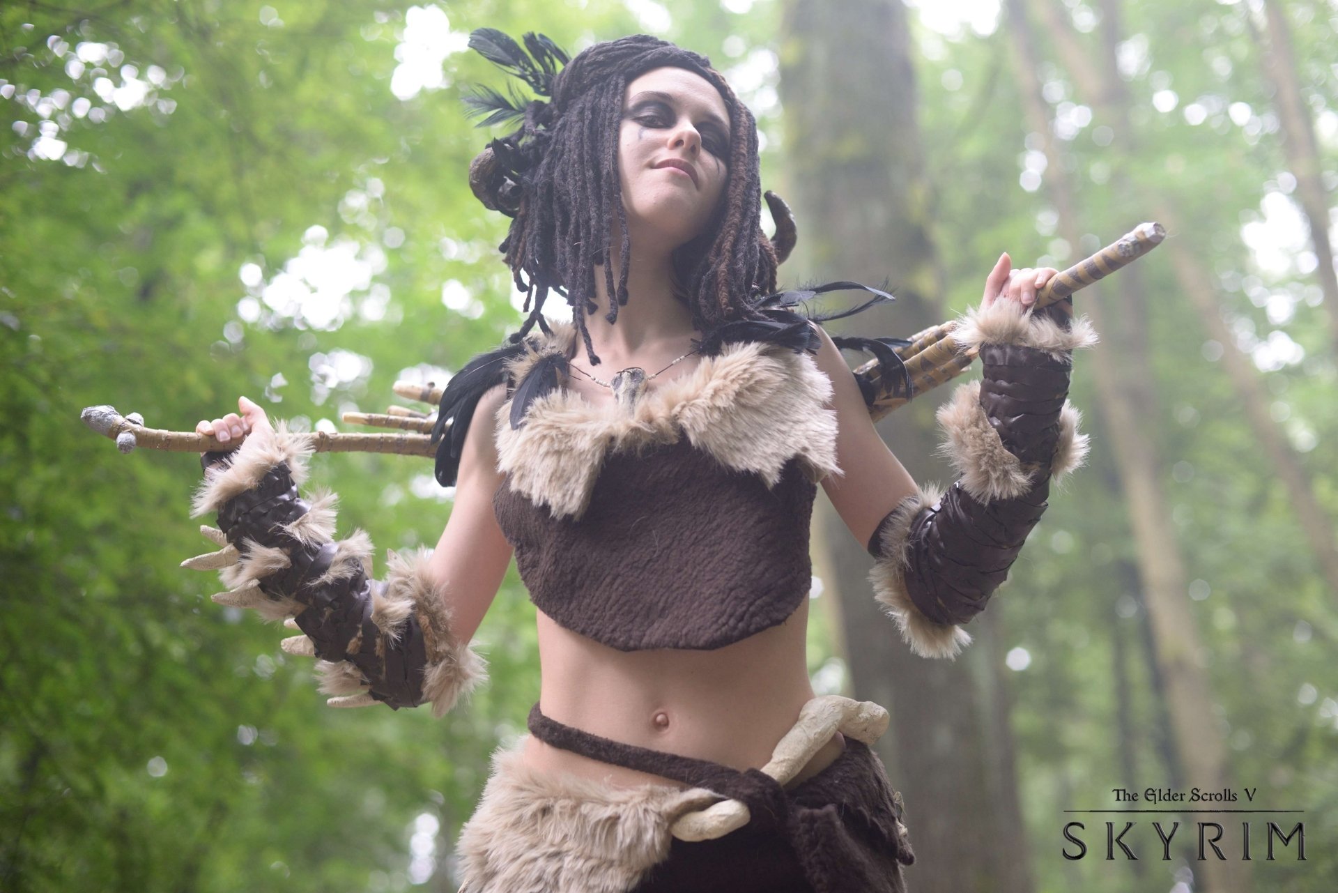 HD PC desktop wallpaper featuring a woman in detailed The Elder Scrolls V: Skyrim cosplay with fur and wooden props, set against a lush forest background.