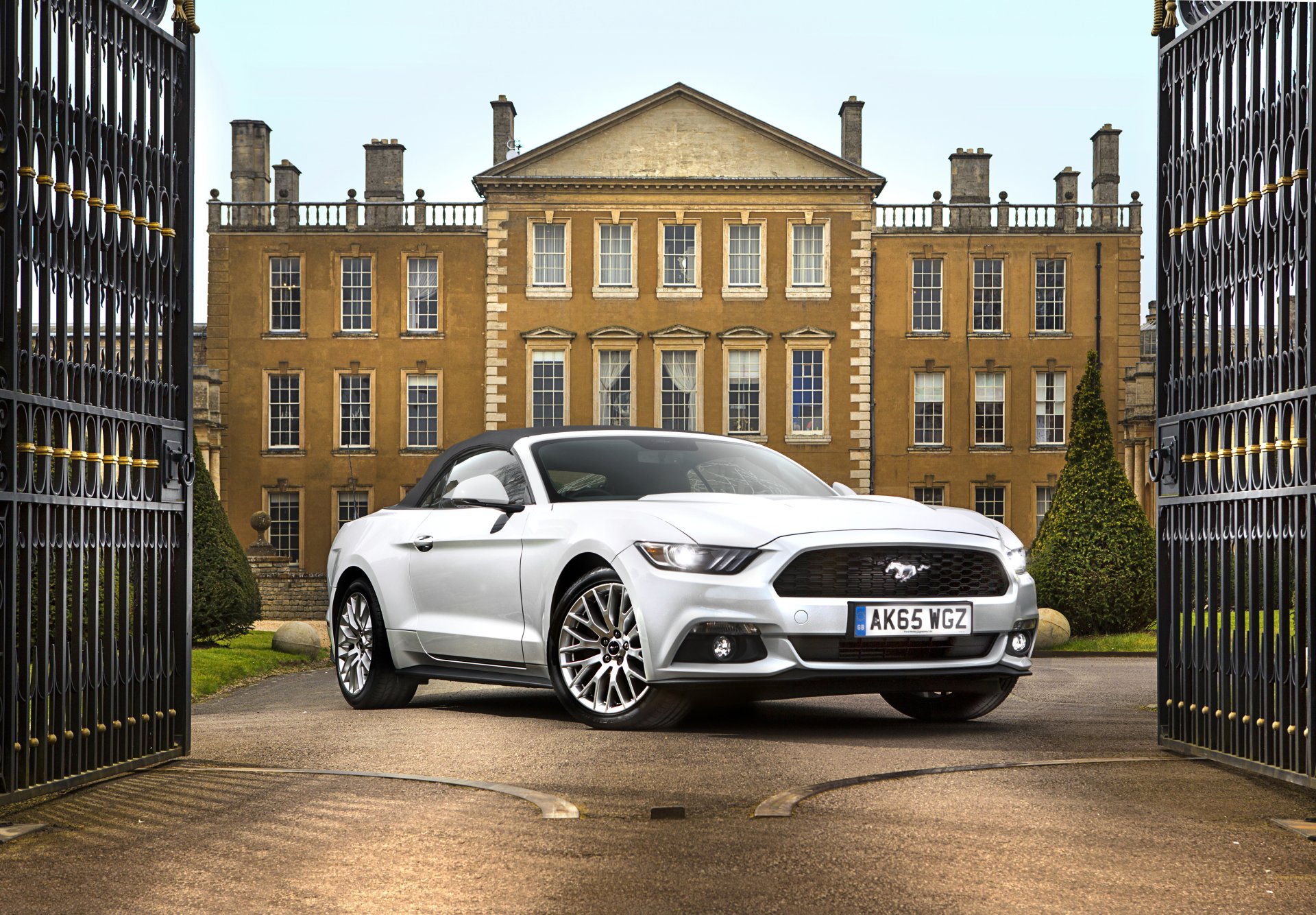 A sleek white Ford Mustang GT parked elegantly in front of a grand estate, framed by ornate gates, depicted in stunning 4K Ultra HD detail.