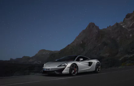 Silver McLaren 570GT supercar parked on a mountain road under a starry night sky, shown in stunning 4K Ultra HD detail.