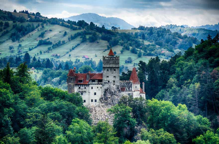 HD wallpaper of Bran Castle, a man-made fortress nestled among lush green hills with misty mountains in the background.