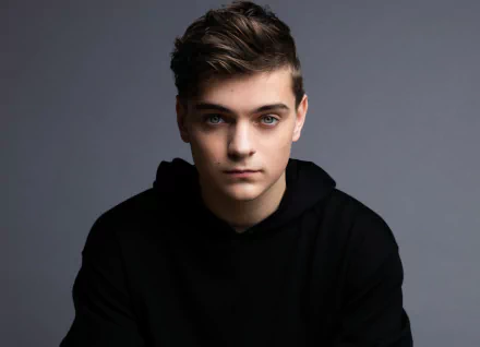 A HD desktop wallpaper featuring DJ Martin Garrix, shown in a black hoodie against a grey background.