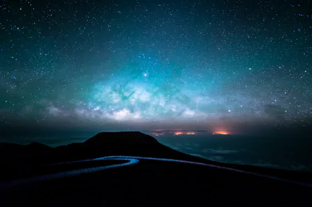 HD wallpaper of a starry night sky featuring the Milky Way above a winding road and hills. The scene captures the beauty of nature under a sky full of stars.