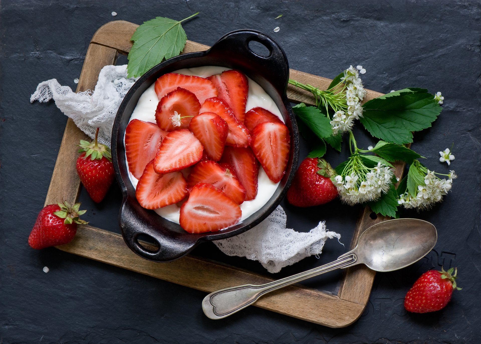 A 4K Ultra HD desktop wallpaper of fresh sliced strawberries atop creamy yogurt in a black bowl, surrounded by whole strawberries and green leaves on a rustic tray.