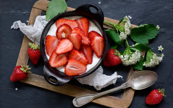 A 4K Ultra HD desktop wallpaper of fresh sliced strawberries atop creamy yogurt in a black bowl, surrounded by whole strawberries and green leaves on a rustic tray.