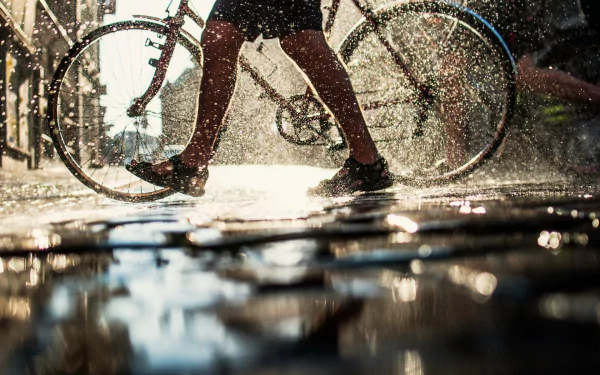 Artistic HD PC desktop wallpaper: sunlit legs and a bicycle splashing through rain-soaked puddles, water droplets sparkling around a walking human.
