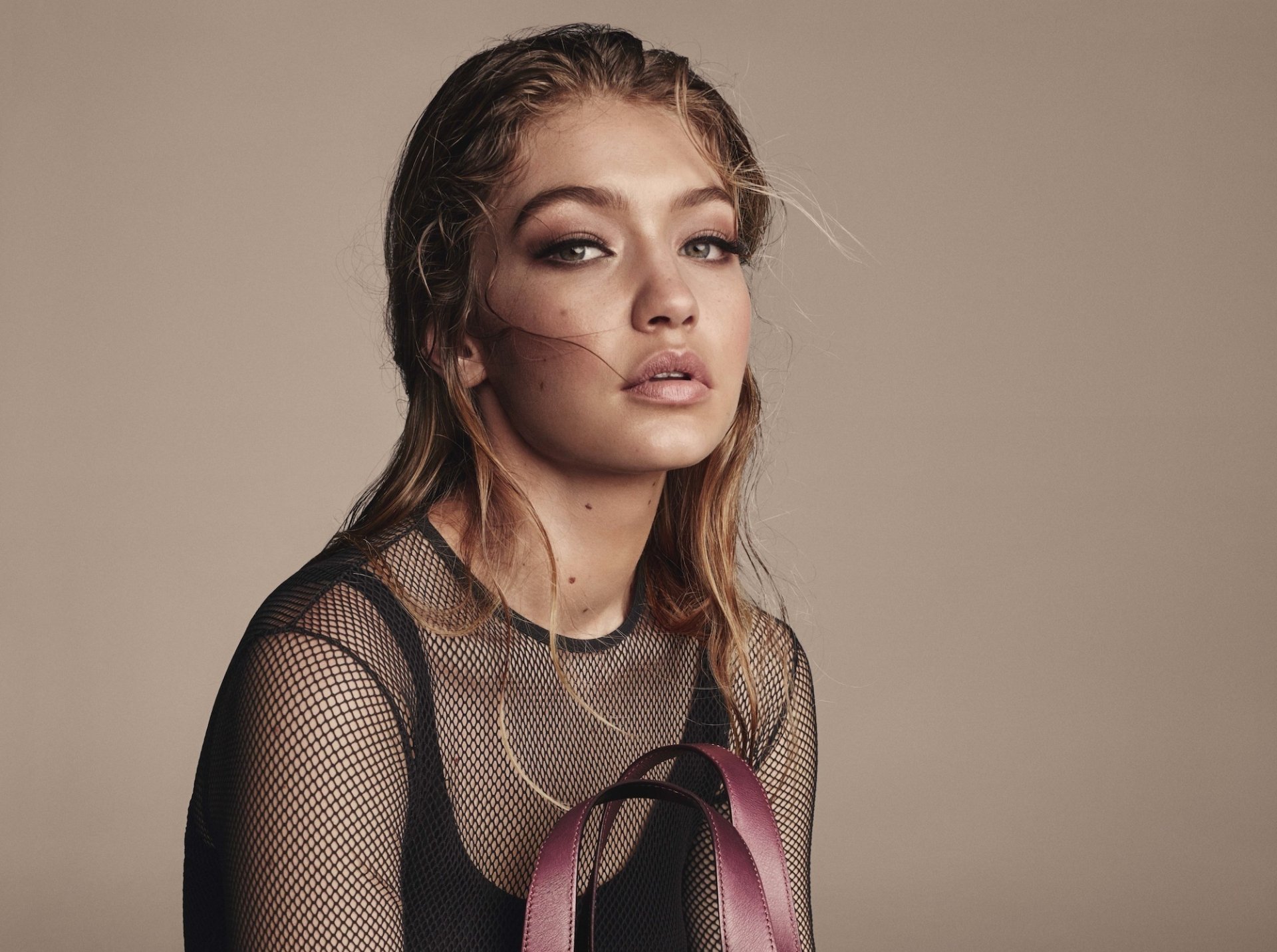 A stunning HD wallpaper featuring Gigi Hadid, an American model, with her blonde hair styled elegantly. The background is neutral, highlighting her expressive gaze and fashion-forward look.