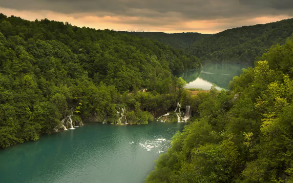 HD PC desktop wallpaper of Plitvice Lakes National Park: emerald lake framed by lush forest and trees with cascading waterfalls.