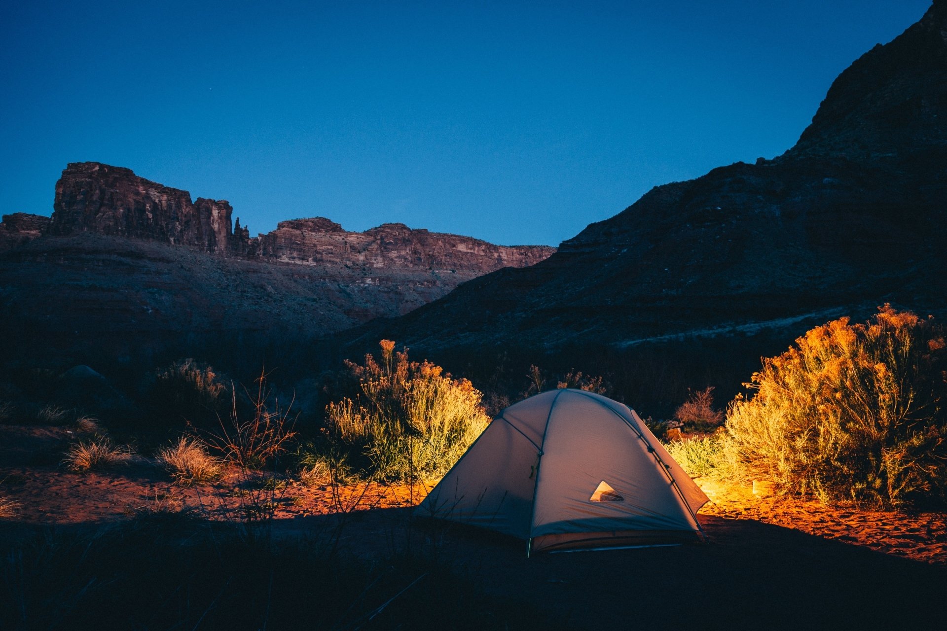 A serene evening scene of a tent illuminated by warm light, set against majestic mountains, capturing the essence of camping and outdoor photography.