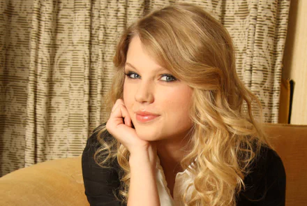 HD desktop wallpaper featuring a close-up portrait of American singer Taylor Swift with blonde hair, posing thoughtfully in a warm indoor setting.