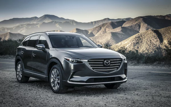 Silver Mazda CX-9 SUV parked on a mountain road, HD desktop wallpaper background showing the Mazda vehicle against rugged hills.