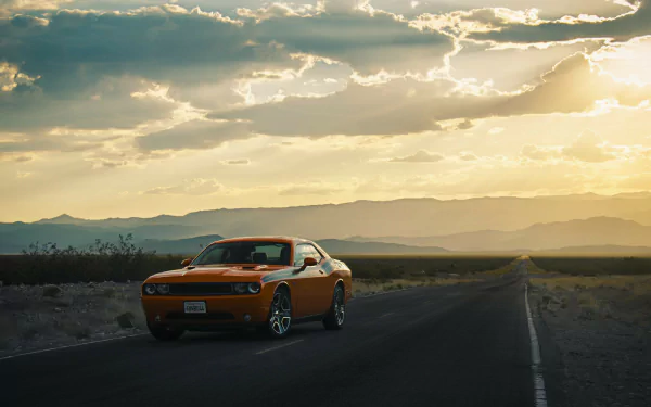 Orange Dodge Challenger vehicle on a desert road at sunset with dramatic clouds and distant mountains — 4K Ultra HD PC desktop wallpaper background.