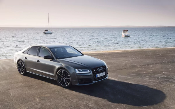A sleek silver Audi A8 parked near the water, with boats in the background, creates a stunning HD wallpaper and desktop background.
