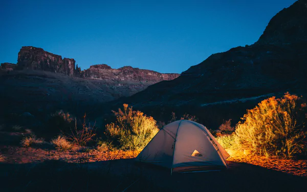 A serene evening scene of a tent illuminated by warm light, set against majestic mountains, capturing the essence of camping and outdoor photography.