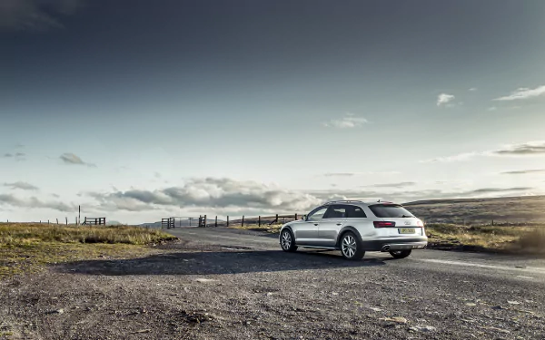 HD desktop wallpaper featuring a silver Audi A6 parked on a rural road under a cloudy sky, showcasing the sleek design of the vehicle in a natural landscape.