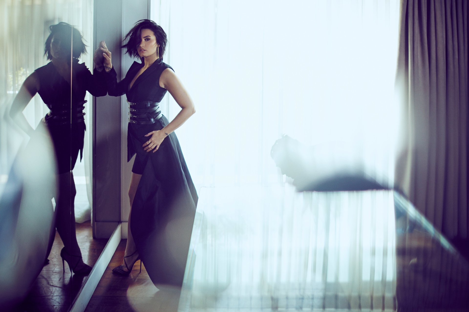 American singer Demi Lovato, a brunette with brown eyes, stands in a black dress beside her reflection in a sleek, modern interior, captured in HD.