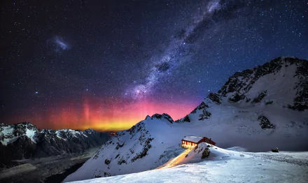A stunning winter landscape features snow-covered mountains beneath a starry sky and the Milky Way, with a warm glow from a cabin illuminating the serene scene.