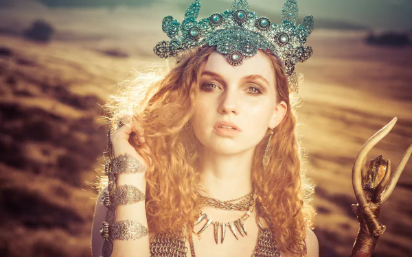 HD desktop wallpaper of redhead model Alexandria Basso wearing an ornate crown and necklace, with green eyes glowing in sunny, warm light.