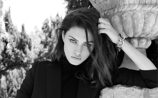 Black and white HD portrait of Australian actress and model Phoebe Tonkin leaning against a stone structure, her brunette hair framing a striking, confident expression.