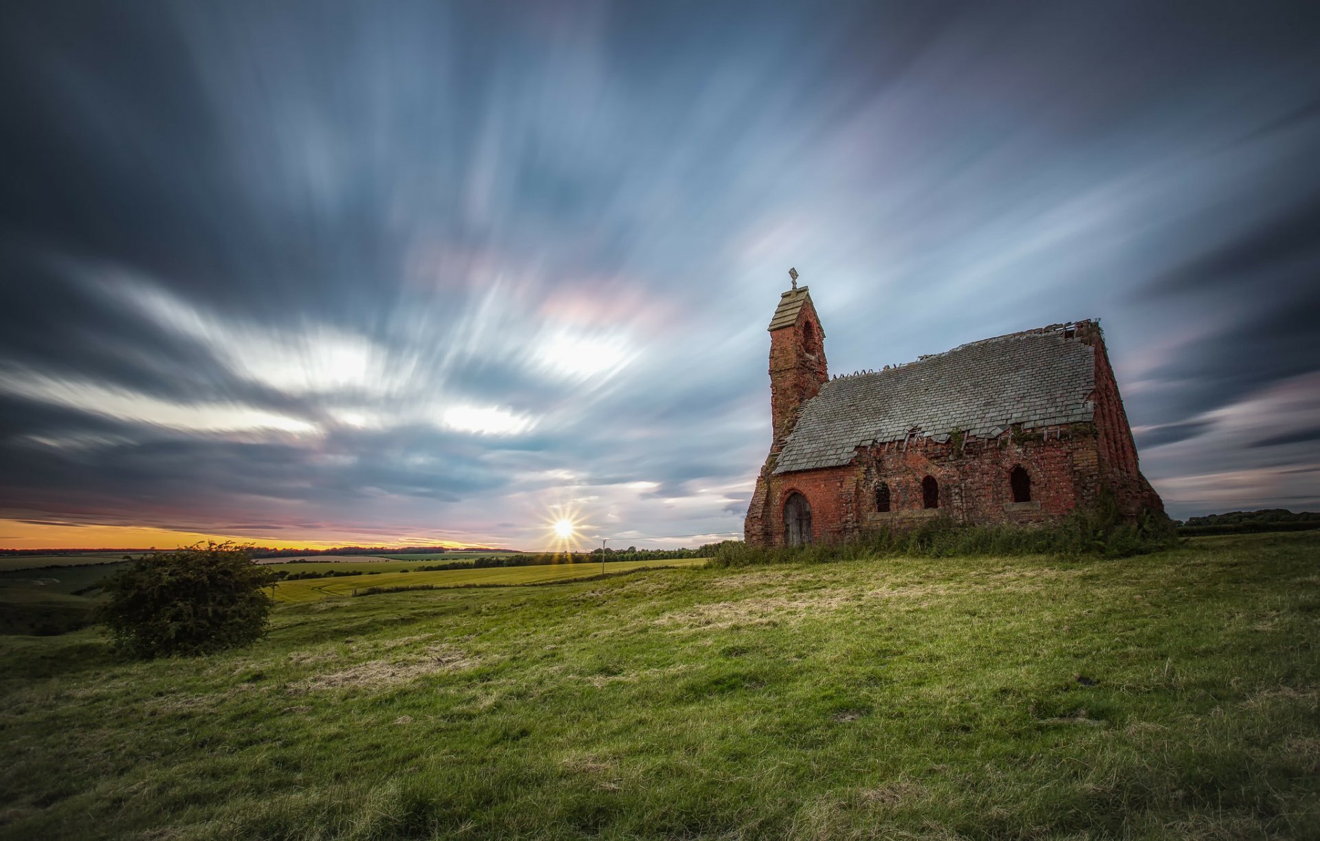 Sunset illuminates a ruined religious chapel set against a dramatic sky over an open English landscape, captured in high definition.
