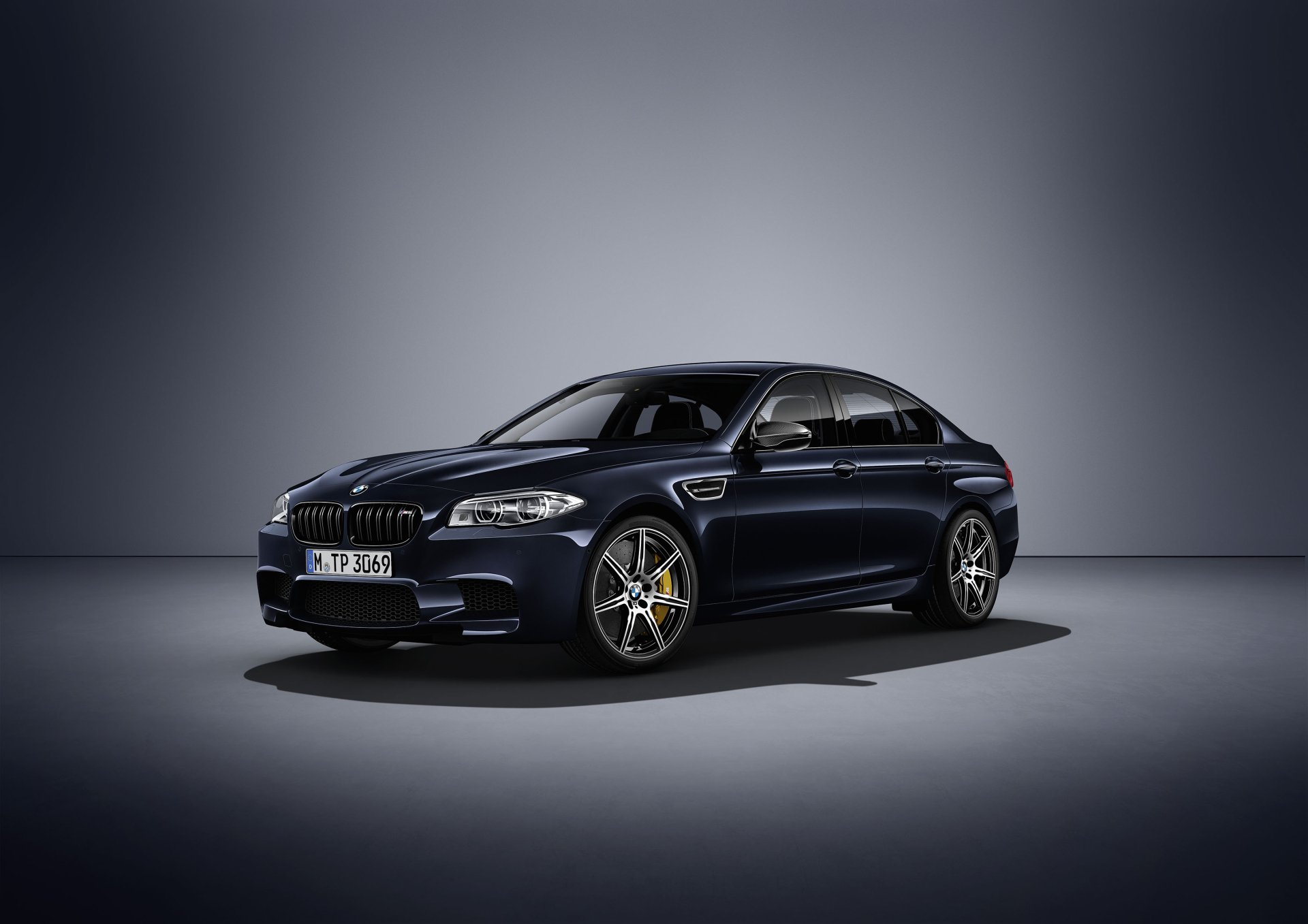 Sleek black BMW M5 sedan on a studio floor, high-detail car/vehicle 2K Quad HD PC desktop wallpaper and background.