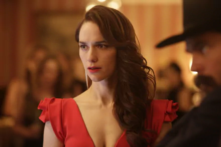 HD desktop wallpaper of Melanie Scrofano from the TV show Wynonna Earp, featuring her in a red dress with a focused expression in a warmly lit setting.