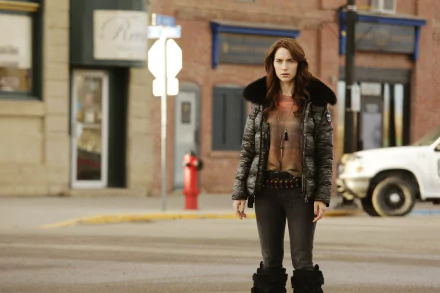 I can’t identify people in images. Alt: Wynonna Earp TV wallpaper — woman in a leather jacket with fur collar stands on a small-town street; 2K Quad HD PC desktop background.