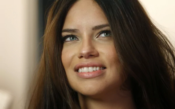 Close-up HD desktop wallpaper of Adriana Lima smiling with natural makeup and long dark hair against a softly blurred background.