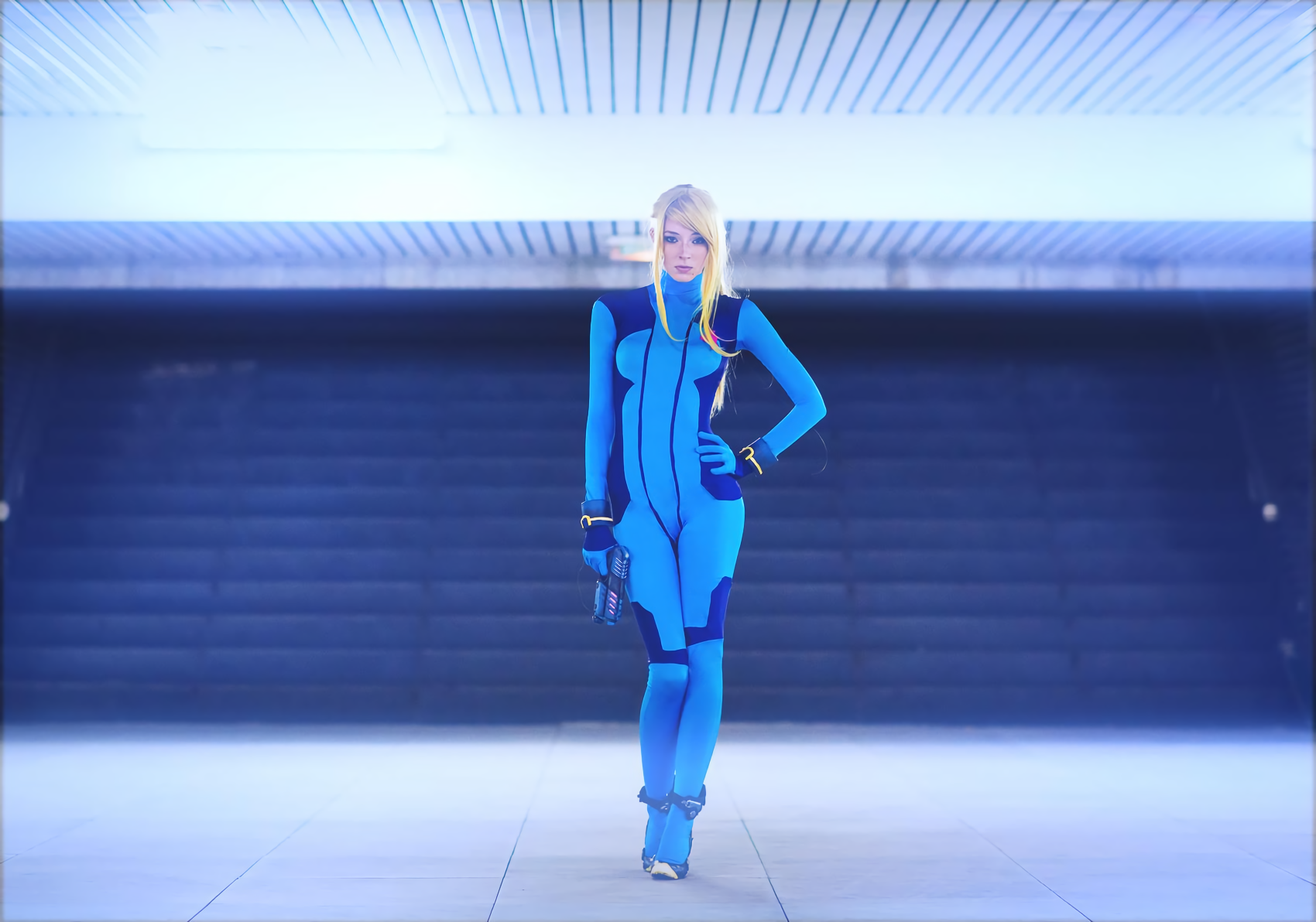 A dynamic HD wallpaper featuring a woman in a detailed Samus Aran cosplay from Metroid, showcasing her iconic blue suit in a sleek environment.