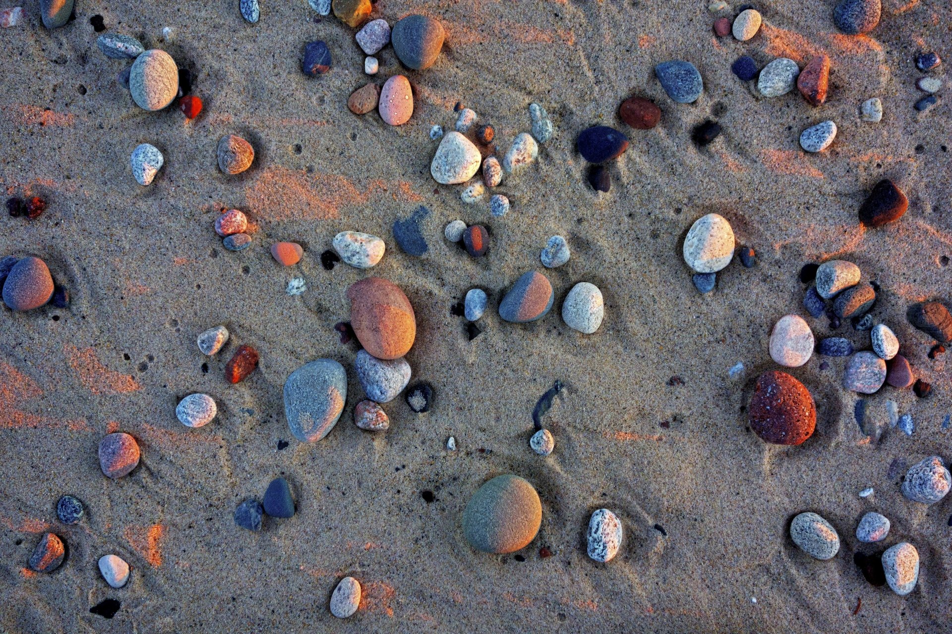 5K Ultra HD PC desktop wallpaper: nature background of smooth stones scattered across rippled sand, warm light casting colorful highlights.