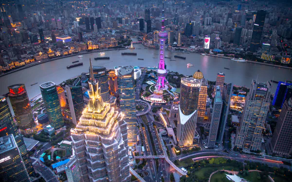 A stunning evening cityscape of Shanghai, showcasing the Oriental Pearl Tower illuminated against a backdrop of skyscrapers and the Huangpu River. Perfect for a HD desktop wallpaper.