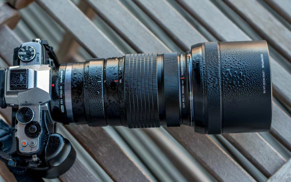 Close-up of an Olympus camera with a detailed man-made lens, showcasing water droplets on the surface, set against a wooden background in this HD desktop wallpaper.