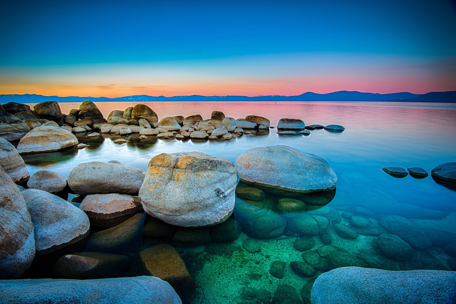 A serene nature scene featuring clear lake waters and smooth rocks under a vibrant, colorful sky, presented as a 4K Ultra HD PC desktop wallpaper.