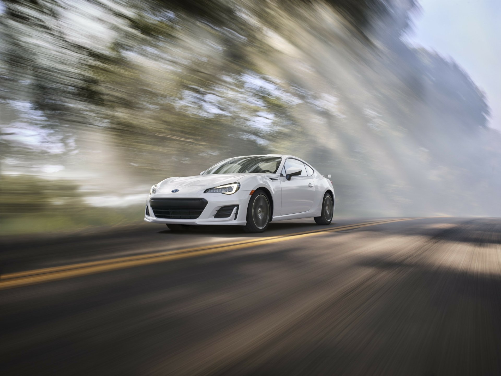 A sleek white Subaru BRZ speeds along a tree-lined road, capturing the essence of dynamic motion in this HD desktop wallpaper.