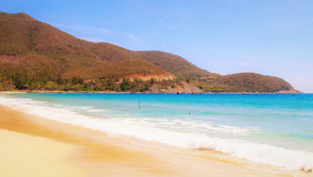 A serene beach scene featuring blue waters and gentle waves, framed by lush green hills under a clear sky, perfect as a stunning 4K Ultra HD desktop wallpaper.