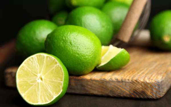 Close-up of fresh green limes, whole and sliced, displayed on a wooden cutting board in vibrant 4K Ultra HD for a vivid PC desktop wallpaper background.