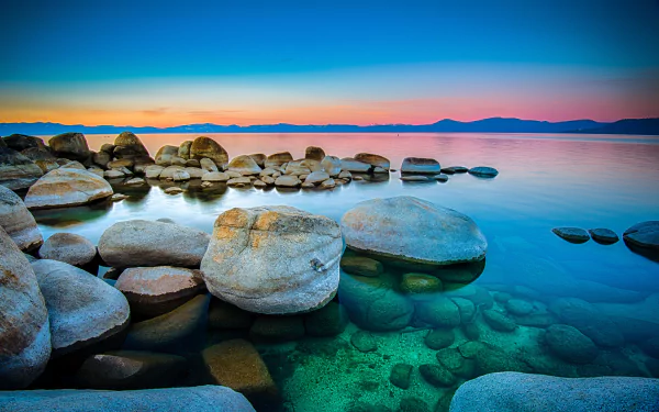 A serene nature scene featuring clear lake waters and smooth rocks under a vibrant, colorful sky, presented as a 4K Ultra HD PC desktop wallpaper.