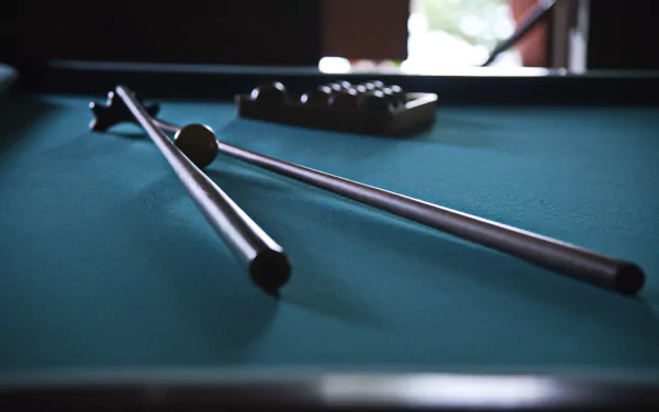 A close-up of pool cues resting on a vibrant green felt table, with a cue ball and a rack of balls in the background, creating an engaging HD PC desktop wallpaper.