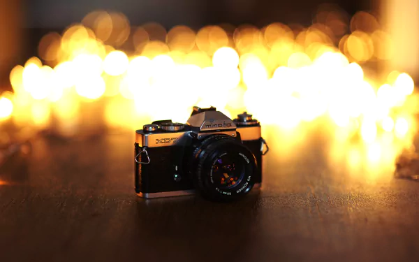 HD desktop wallpaper featuring a Minolta camera with warm bokeh lights in the background, blending man-made design and artistic photography.