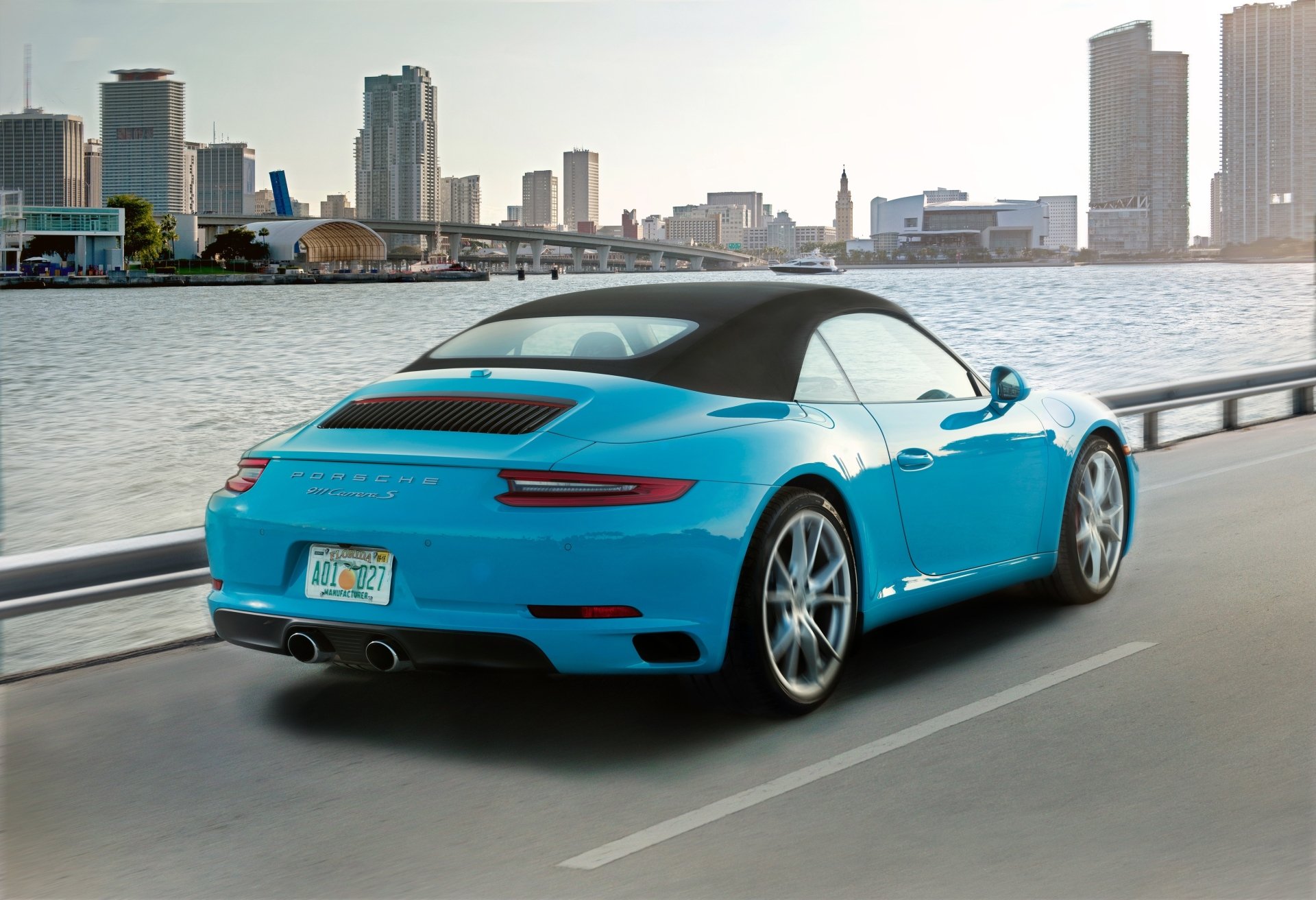 Bright blue Porsche 911 Carrera sports car driving along a waterfront skyline — 4K Ultra HD PC desktop wallpaper of a Porsche 911 vehicle.