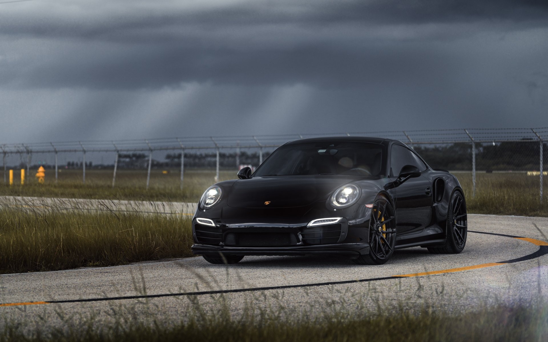 Black Porsche 911 Carrera driving on a curved road under a moody sky, captured in a 4K Ultra HD PC desktop wallpaper.