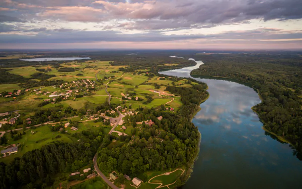 Aerial panorama of a river winding through a lush forest and countryside in Lithuania under a cloudy sky, captured in HD landscape photography.