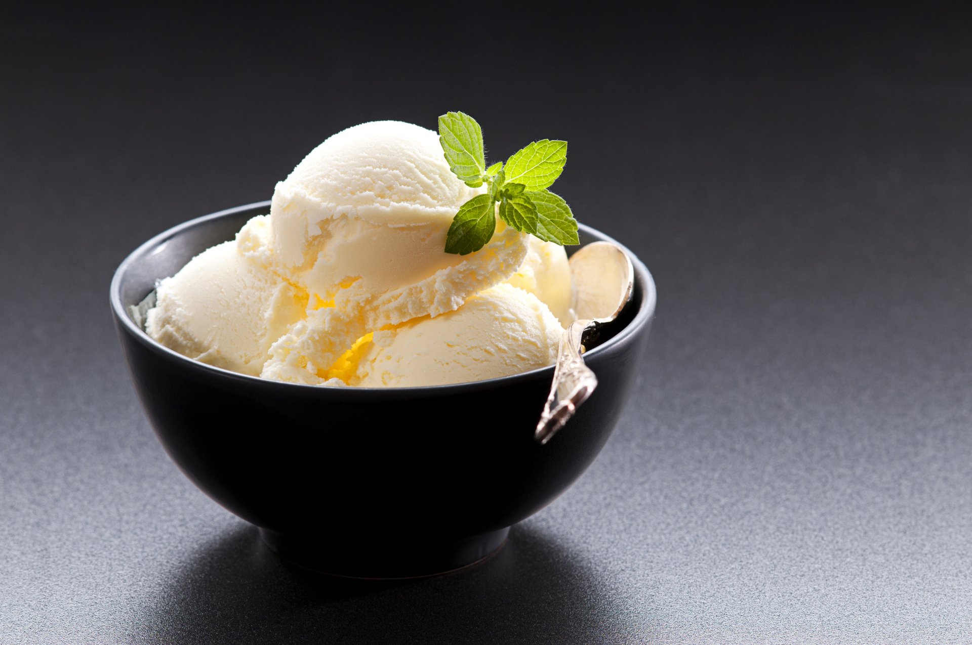 A black bowl filled with scoops of creamy vanilla ice cream garnished with fresh mint leaves, captured in stunning 4K Ultra HD as a PC desktop wallpaper.