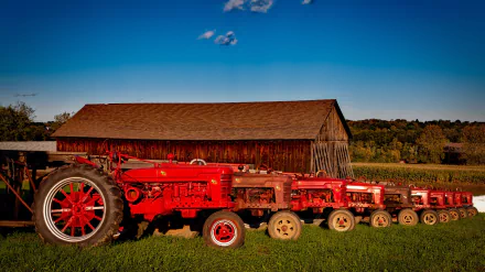 HD PC desktop wallpaper of an old red vintage Farmall tractor with extra wheels parked on grass before a weathered barn under a blue sky
