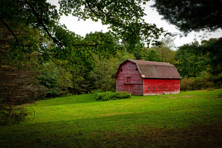 A red barn set in the lush green countryside of Connecticut, USA, surrounded by trees under a partly cloudy sky.