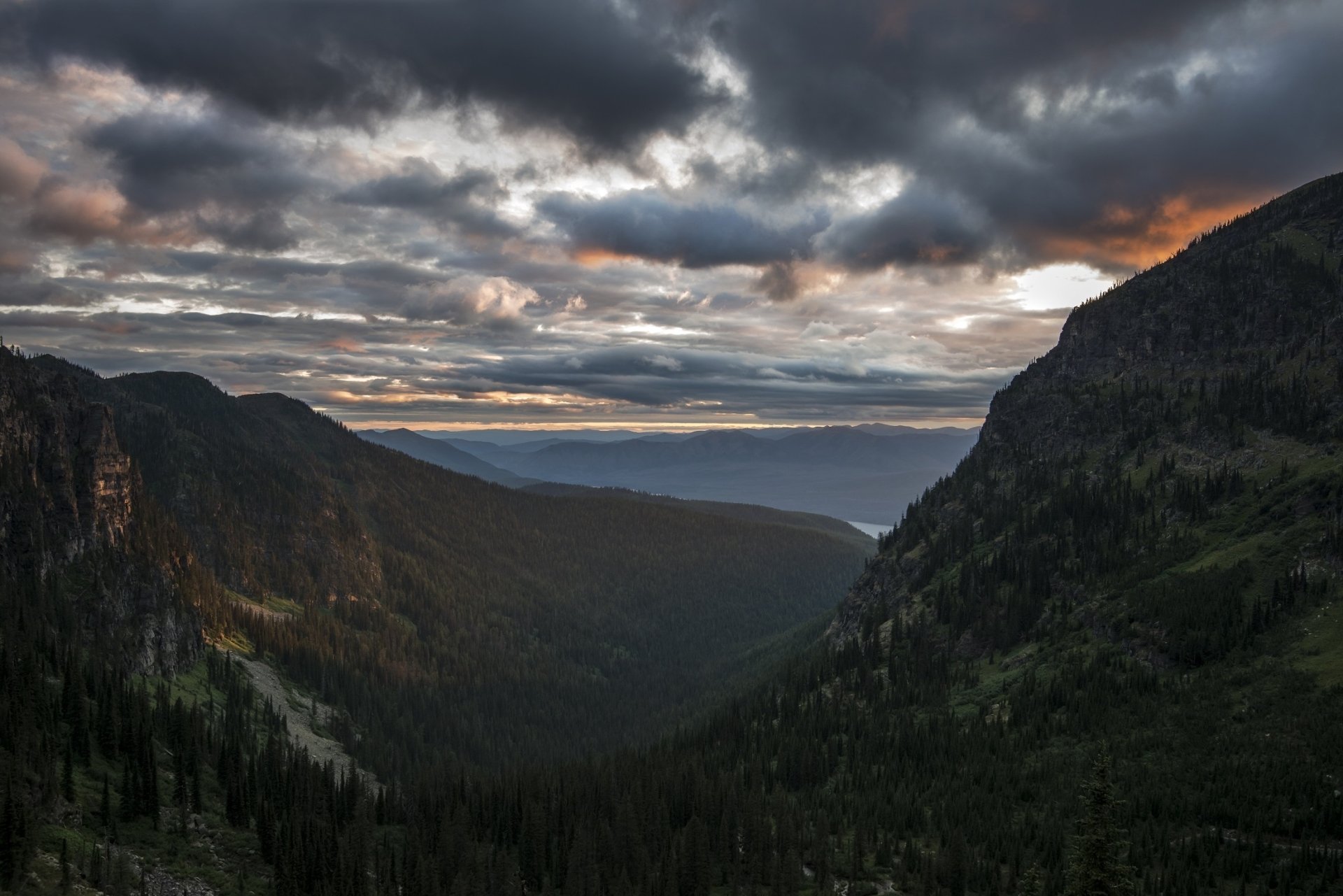Dusk settles over a scenic mountain landscape with trees silhouetted against a dramatic sky filled with clouds, captured in a high-definition PC desktop wallpaper.