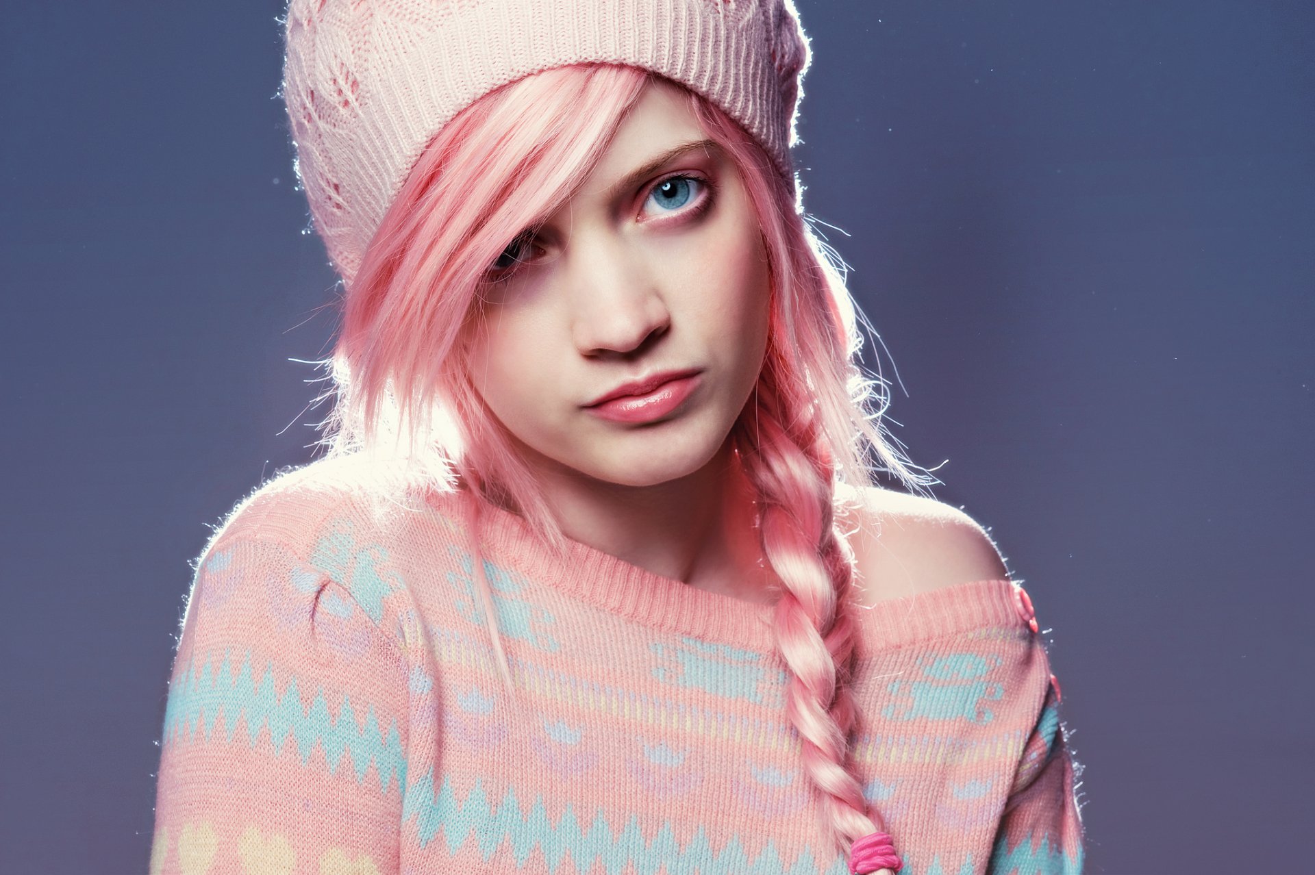 A woman with pink braided hair and blue eyes wears a cozy sweater and a hat, creating a striking backdrop for a vibrant HD desktop wallpaper.
