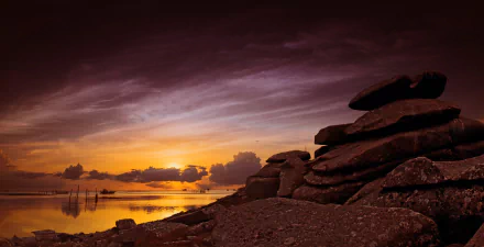 4K Ultra HD desktop wallpaper featuring a dramatic coastal landscape at sunset with dark rocks in the foreground and calm ocean waters under a colorful sky.