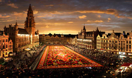 A stunning HD desktop wallpaper of Brussels' Grand Palace in Belgium, showcasing its intricate architecture and vibrant floral carpet under a dramatic sunset sky.