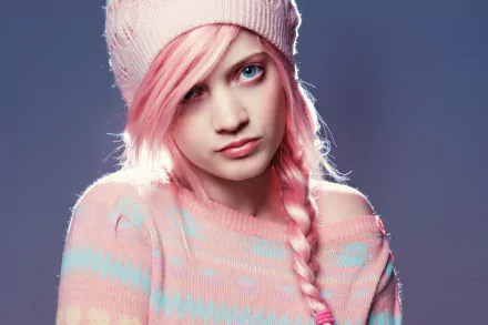 A woman with pink braided hair and blue eyes wears a cozy sweater and a hat, creating a striking backdrop for a vibrant HD desktop wallpaper.